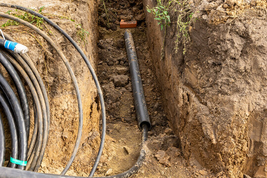 Underground cable installation with protective plastic pipe and red brick for mechanical damage prevention in clay soil trench