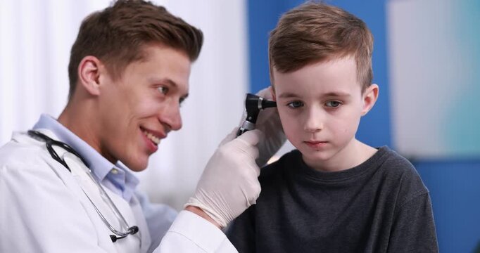 Hearing test. Doctor examining boy's ear with otoscope in clinic. Camera spinning