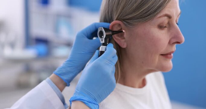 Hearing test. Doctor examining woman's ear with otoscope in clinic, closeup