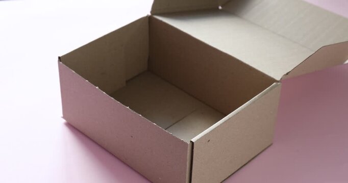 Woman putting shredded paper filler into cardboard box at pink table, closeup