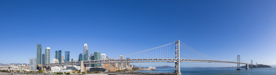 Obraz premium A wide panoramic view of the San Francisco skyline featuring the Bay Bridge, financial downtown center and city waterfront, USA.