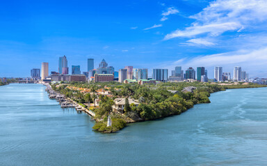 Fototapeta premium Aerial view of Tampa, Florida, featuring a lush waterfront peninsula with luxury homes, private docks, a small lighthouse, and the downtown city skyline in the background