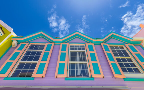 Low angle view of a vibrant purple and turquoise colonial building with decorative zigzag roofline and teal window frames in Philipsburg, Sint Maarten, against a bright blue sky