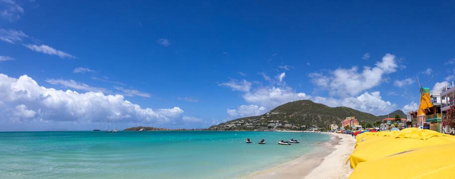 Wide panoramic view of the beach at Great Bay in Philipsburg Sint Maarten featuring numerous yellow umbrellas turquoise water and a green mountain coastline