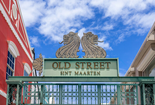 Colorful decorative Old Street Sint Maarten entrance gate with twin lion sculptures and ornate green ironwork in Philipsburg, flanked by colorful colonial buildings under a blue sky