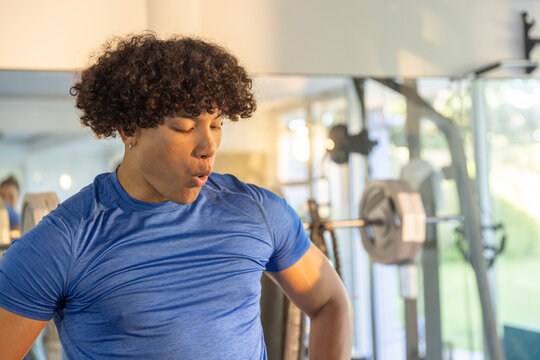 Adult male wearing blue athletic tee standing in gym with mirrored wall and loaded squat rack