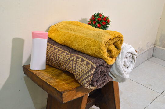 Looking down from a quarter left angle at neatly arranged towels and skin moisturizing lotion next to a small artificial flower pot on a curved wooden stool.