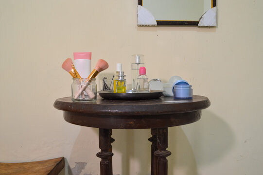 A centered shot of a bedroom vanity table filled with liquid skincare bottles, a set of professional makeup brushes, lipsticks, and manicure tools organized neatly for a daily beauty routine.
