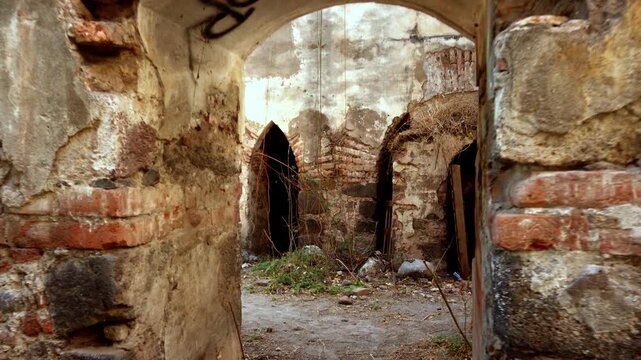 View of deteriorated hacienda structure with cracked walls and brick arches, abandoned doorways and debris on ground, historic architecture showing decay and passage of time