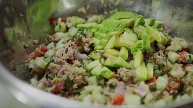 Closeup view of tuna ceviche with chopped vegetables and avocado being mixed in bowl, vibrant ingredients and textures showing fresh seafood preparation and healthy homemade meal