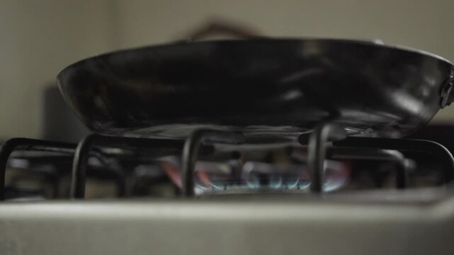 Empty frying pan heating over an active gas burner with visible blue flame in a kitchen setting.