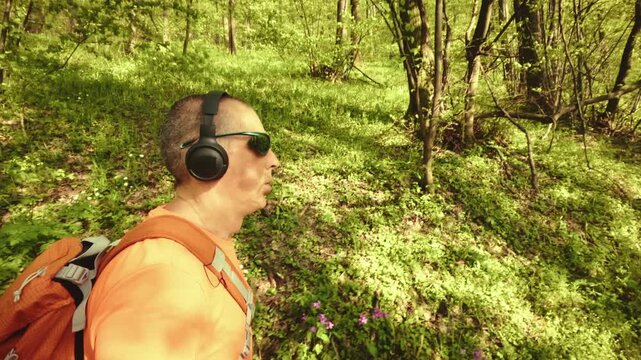 High-quality 4k b-roll footage of an active mature man (50+) with a backpack and headphones running, hiking, and walking on a forest trail. Concept of healthy aging, active lifestyle.