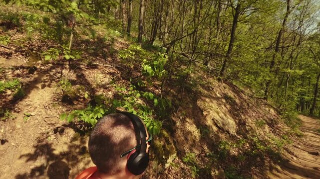 High-quality 4k b-roll footage of an active mature man (50+) with a backpack and headphones running, hiking, and walking on a forest trail. Concept of healthy aging, active lifestyle.