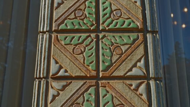 Extreme close-up static shot of glazed ceramic tiles on a historic building column, green leaf and acorn relief pattern within geometric frames, warm sidelight emphasizing carved texture and depth.