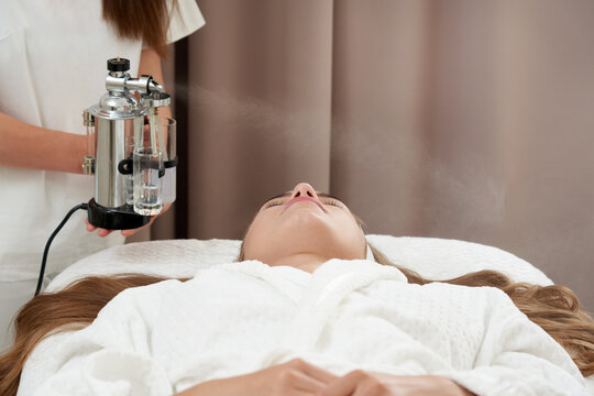 The procedure of steaming the skin of the face of a young woman before cleaning the skin in a cosmetology salon