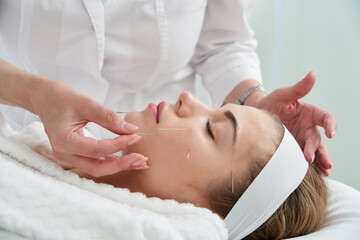 Fototapeta premium Young woman having an acupuncture treatment therapy on her face in spa salon. Alternative medicine and therapy concept