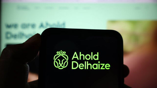 Closeup of a smartphone screen displaying the ahold delhaize corporate logo in green against a dark background, held in a hand