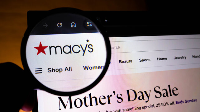 Magnifying glass held over a computer screen showing the macys website logo and mothers day sale advertisement