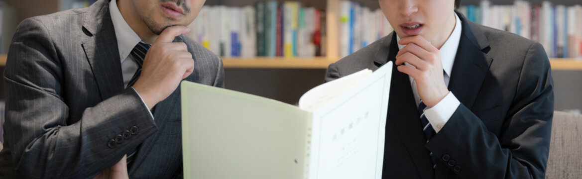 本棚のある社長室で資料を見ながら相談、ビジネスマンの打ち合わせ　決算報告などの会計士や士業のイメージ困る考える悩むイメージ「m＆aしたいけど粉飾決算&hellip;？」顔無しバナー