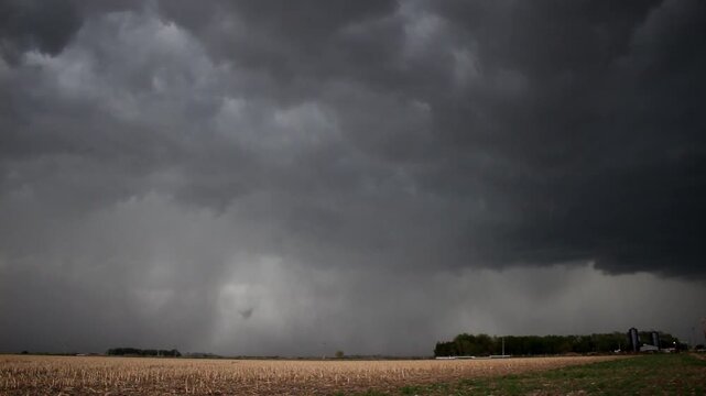 Time lapse of swirling storm clouds and rain falling over farmland.