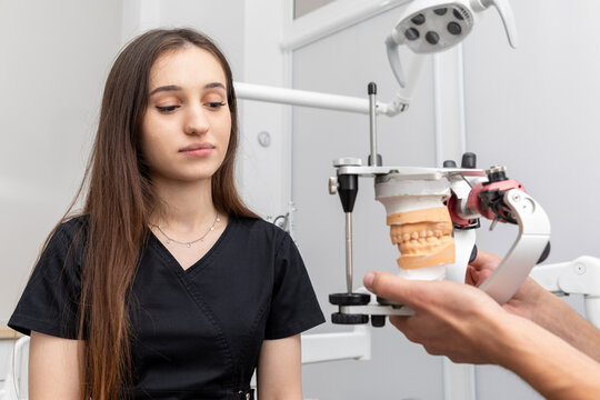 Dentist holding dental articulator with dental gypsum prosthesis model showing it to a patient