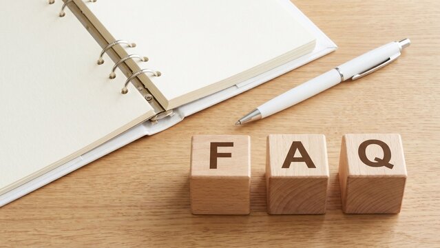 木製デスクの上に並んだFAQの文字入りウッドブロックと白いノート、ペンを組み合わせた、よくある質問・問い合わせ対応・カスタマーサポート・情報整理を表現するビジネスイメージ