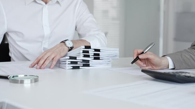 Professionals handling a large stack of documents and paperwork, signing a contract in a busy office. Audit and taxes in business