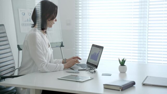 Professional woman crunching numbers and analyzing financial data on a laptop in a bright modern office, planning business strategies and managing growth