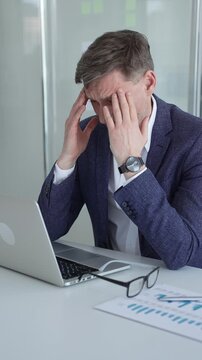Businessman slumped at his office desk, rubbing his temples from headache and digital eye strain, exhausted and overwhelmed by work pressure and professional burnout
