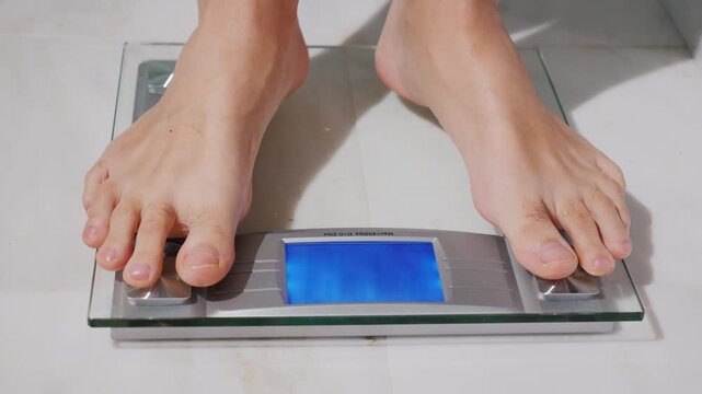 Man standing on digital bathroom scales to check body weight in bright room close up of bare feet on glass electronic device for health monitoring tracking fitness progress and daily wellness habits.
