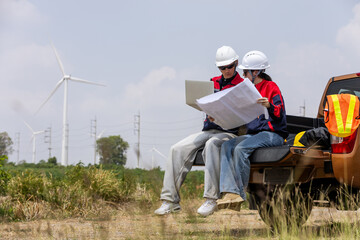 Engineers checking blueprint on pickup truck at wind turbine farm, working on renewable energy project planning and site inspection. Clean power, field operation, teamwork, sustainability concept. © eakgrungenerd
