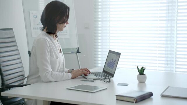Professional woman crunching numbers and analyzing financial data on a laptop in a bright modern office, planning business strategies and managing growth