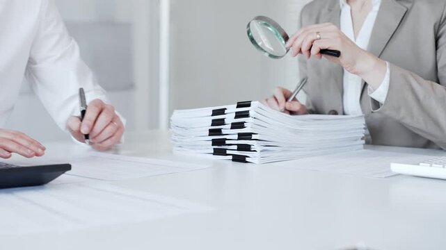 Business professionals auditing financial documents with a magnifying glass, reviewing paperwork for analysis and investigation. Audit and taxes in business