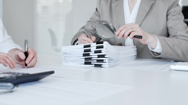 Business professionals auditing financial documents with a magnifying glass, reviewing paperwork for analysis and investigation. Audit and taxes in business