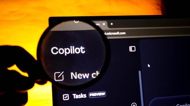 Closeup of a magnifying glass focusing on the microsoft copilot logo on a computer screen, representing ai technology and digital search tools