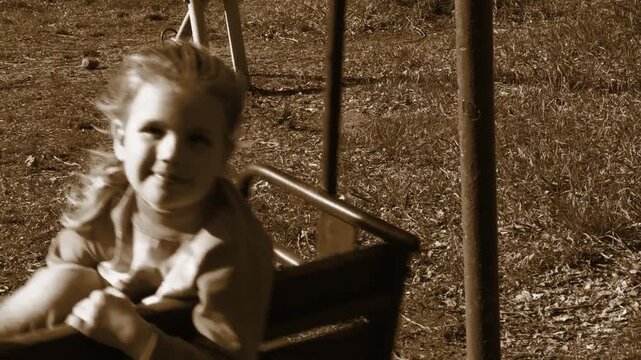 Happy pretty young girl on swings, old quite park. Healthy activity for children. Retro style creating authentic mood. The scene exudes authenticity and the simple joys of childhood. Nostalgia