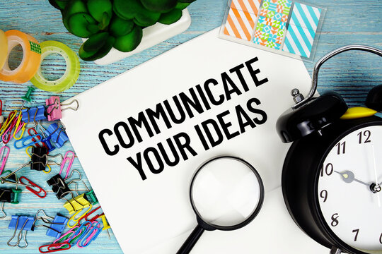 Communicate Your Ideas text on a paper surrounded by office supplies, a magnifying glass, and a clock on a blue wooden surface