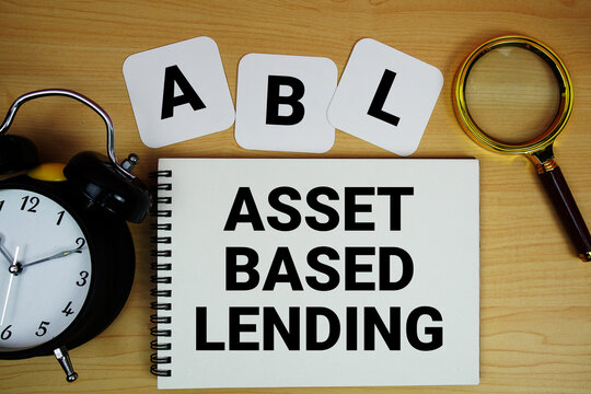 ABL Asset Based Lending text written on notepad with magnifying glass and alarm clock on wooden background