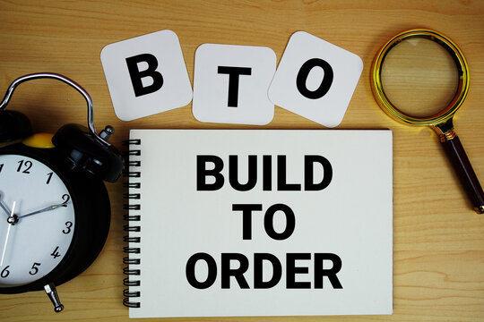 BTO Build to Order text written on notepad with magnifying glass and alarm clock on wooden background