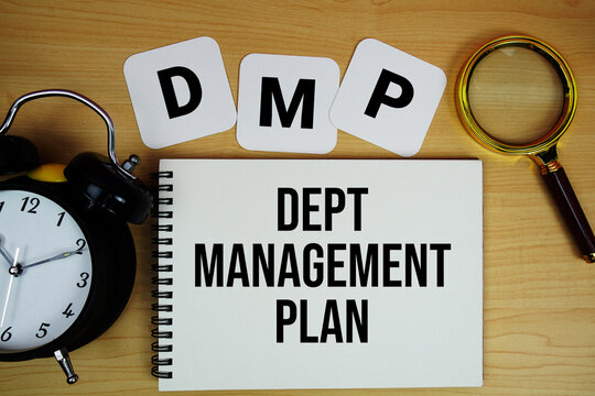 DMP Dept Management Plan text written on notepad with magnifying glass and alarm clock on wooden background