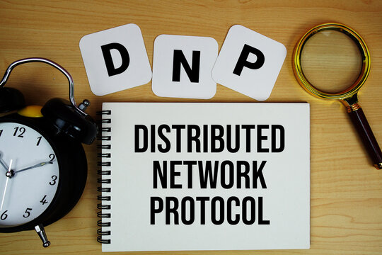DNP Distributed Network Protocol text written on notepad with magnifying glass and alarm clock on wooden background