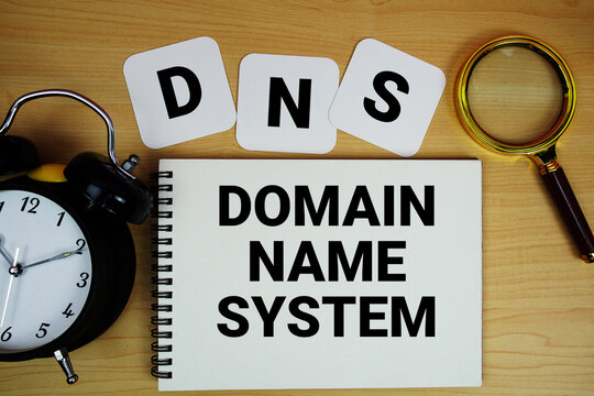 DNS Domain Name System text written on notepad with magnifying glass and alarm clock on wooden background
