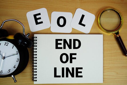 EOL End of Line text written on notepad with magnifying glass and alarm clock on wooden background