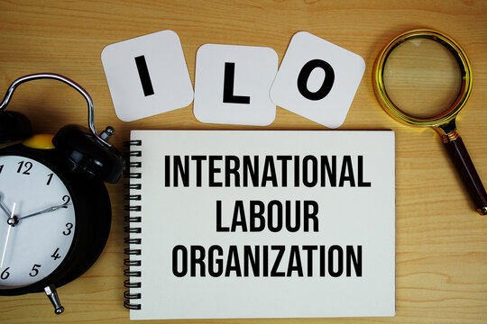 ILO International Labour Organization text written on notepad with magnifying glass and alarm clock on wooden background
