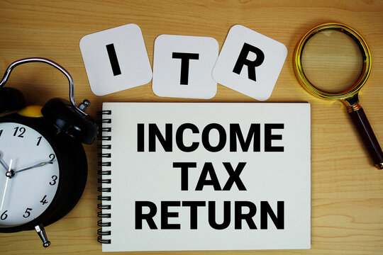 ITR Income Tax Return text written on notepad with magnifying glass and alarm clock on wooden background