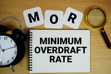 MOR Minimum Overdraft Rate text written on notepad with magnifying glass and alarm clock on wooden background © may1985