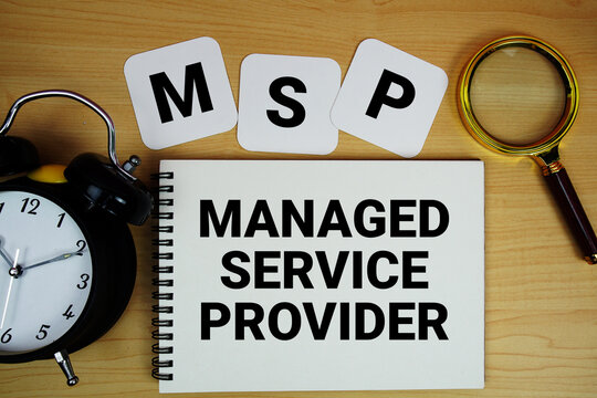 MSP Managed Service Provider text written on notepad with magnifying glass and alarm clock on wooden background