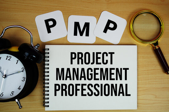 PMP Project Management Professional text written on notepad with magnifying glass and alarm clock on wooden background