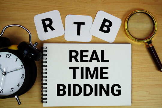 RTB Real Time Bidding text written on notepad with magnifying glass and alarm clock on wooden background