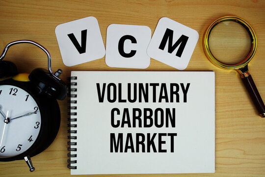 VCM Voluntary Carbon Market text written on notepad with magnifying glass and alarm clock on wooden background